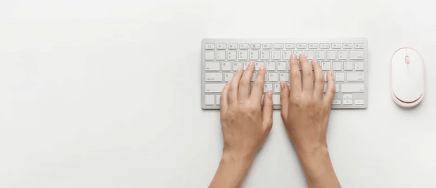 Des mains sur un clavier d'ordinateur. Une souris est à côté.
