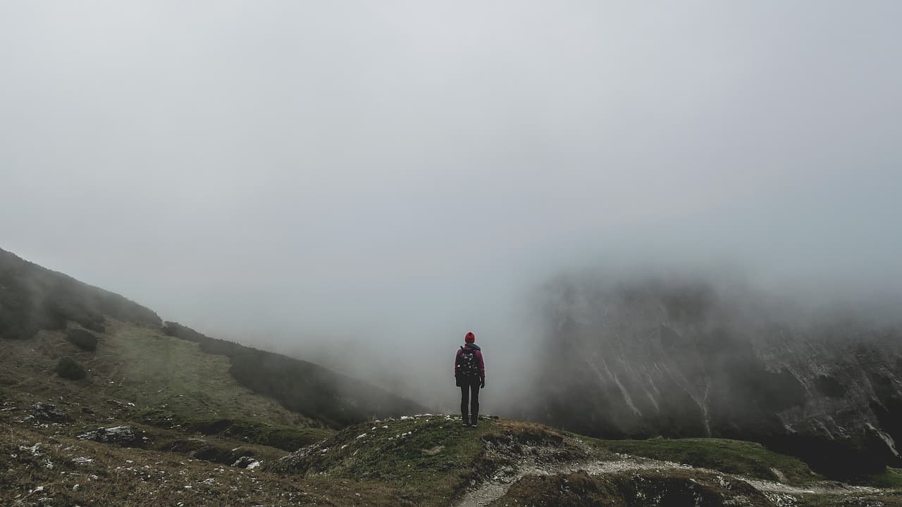 Une personne de dos sur un chemin de montagne, face à un épais brouillard ne permettant pas de savoir où avancer. Crédits en pied de page.